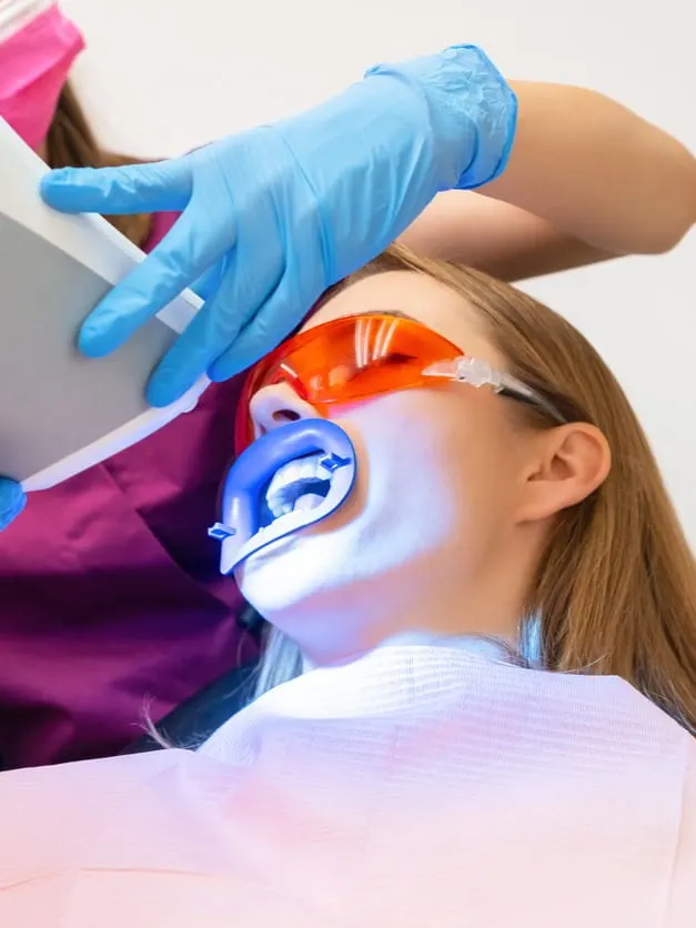 Dentysta wybiela pacjentowi zęby specjalną lampą.